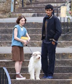 a man standing next to a woman on the steps with a white dog in front of him