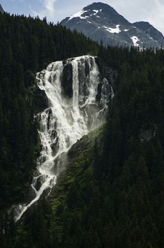 a large waterfall in the middle of a forest with snow on it's top