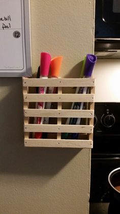 a wooden crate holding pens and markers on the wall next to a stove top oven