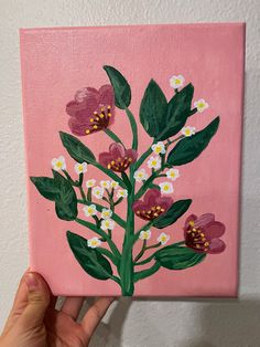 a hand is holding up a pink painting with flowers on the bottom and green leaves