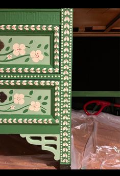 a green dresser with flowers painted on it and some plastic bags next to the drawers