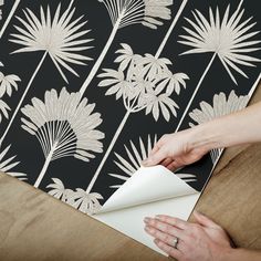 a woman is wrapping up a wallpaper with white flowers and leaves on black background