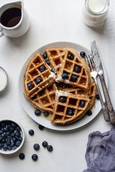 a plate with waffles and blueberries on it next to cups of coffee