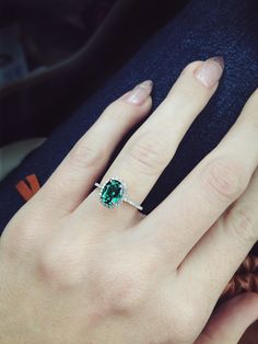 a close up of a person's hand with a green ring on their finger