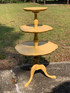 three tiered yellow cake stand sitting in the middle of a yard with grass behind it