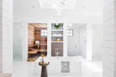 a bathroom with white walls and flooring has a bathtub in the center, along with a wooden shelf