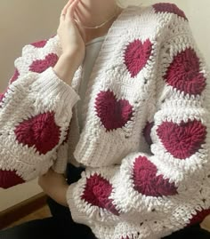 a woman wearing a white and red crocheted jacket with hearts on it sitting in a chair