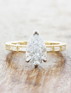 a pear shaped diamond engagement ring on top of a wooden table with gold trimmings