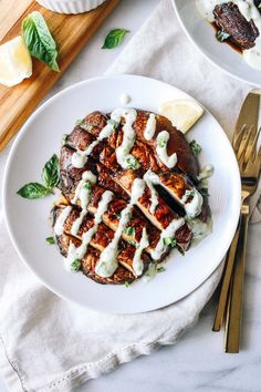 two white plates topped with meat covered in sauce and garnished with green leaves