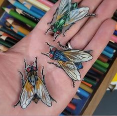 two bees on the palm of someone's hand with colored pencils in the background