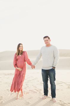 a pregnant couple holding hands while standing in the sand