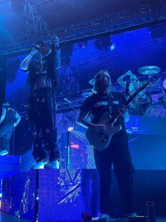 two men standing on stage with guitars in their hands and one man playing the guitar