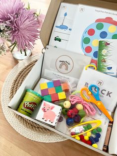 a box filled with lots of toys on top of a wooden table next to a vase