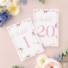 the table numbers are pink and white with flowers around them on a light pink background