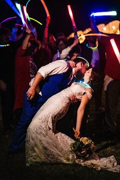 a bride and groom kissing in front of their wedding party with glowing hula hoopers