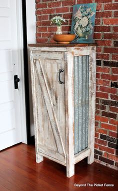 an old white cabinet sitting in front of a brick wall next to a potted plant