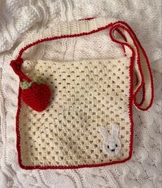 a crocheted bag with a red handle and an apple on the front, sitting on a white blanket