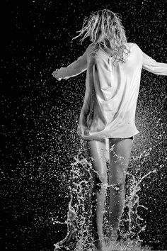 a woman standing in the water with her arms spread out and splashing all over her