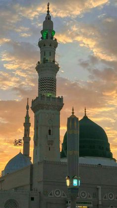 a tall white building with a green light on top and clouds in the background at sunset