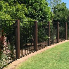 a black fence is next to a grassy area with trees and bushes in the background