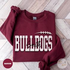 a maroon sweatshirt with the word bulldogs written on it and a football in white letters