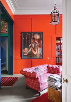 a living room with an orange wall and pink couch in front of a painting on the wall