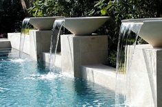 three large water fountains are in the middle of a pool with blue water flowing from them