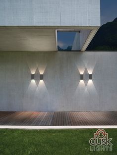 three lights on the side of a building with grass in front of it and a wooden floor