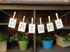 there is a sign that says drinks hanging on the clothesline next to potted plants