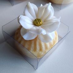 there is a cupcake with a flower on it sitting in a clear box next to other pastries