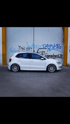 a white car parked in front of a building with graffiti on the wall behind it