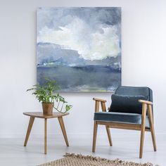 two chairs and a table in front of a painting on the wall with a plant