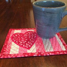 a blue mug sitting on top of a table next to a red heart coaster and a cup holder