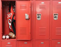 the lockers are red and there is a football jersey hanging on one side of the locker