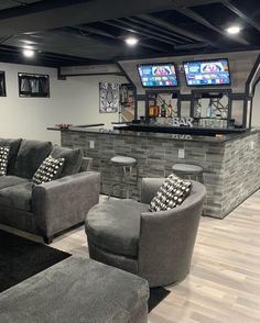 a living room filled with furniture and two tvs on top of a wall next to a bar