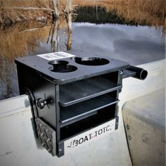 an old fashioned stove sitting on the side of a boat near some water and reeds