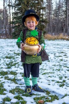 a little boy dressed in green and black holding a pot with gold coins on it