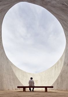 a man sitting on a bench in front of a large circular structure