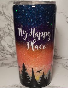 a tumbler with the words, my happy place painted on it and pine trees