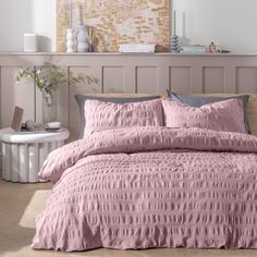 a bed with pink comforter and pillows in a room next to a window,