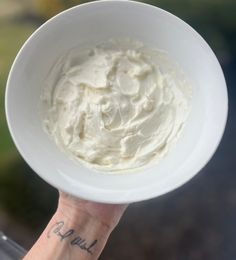 a hand holding a white bowl with whipped cream in it's center and writing on the side