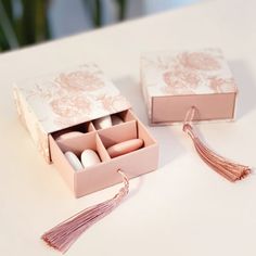 two pink boxes with tassels are sitting on a white table top and one is open