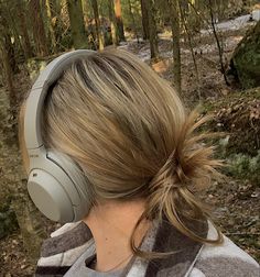 a woman with headphones on in the woods looking at something behind her back to the camera