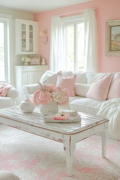 a living room with pink walls and white furniture in the center table is a coffee table that has flowers on it