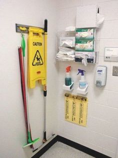 there is a yellow caution sign hanging on the wall next to cleaning supplies and brooms