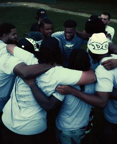 a group of young men hugging each other in a huddle on the grass at night