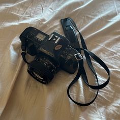 a black camera sitting on top of a bed next to a white sheet with a strap around it