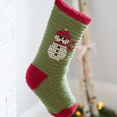 a crocheted christmas stocking hanging from a hook on the wall next to a tree