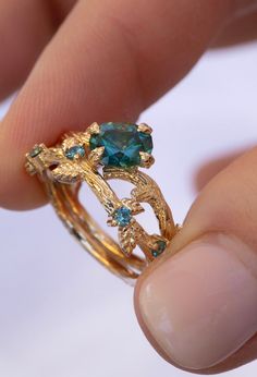 a close up of a person's hand holding a gold ring with blue stones