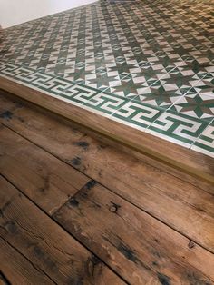 a wooden floor with green and white tiles on it's sides, next to a wall